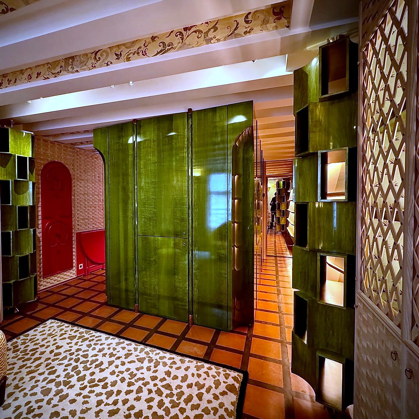 Vue large de l'agencement : placards toute hauteur en sycomore vernis haut brillant, bibliothèque tournante, chaises Tallon et table basculante en laque rouge satinée
